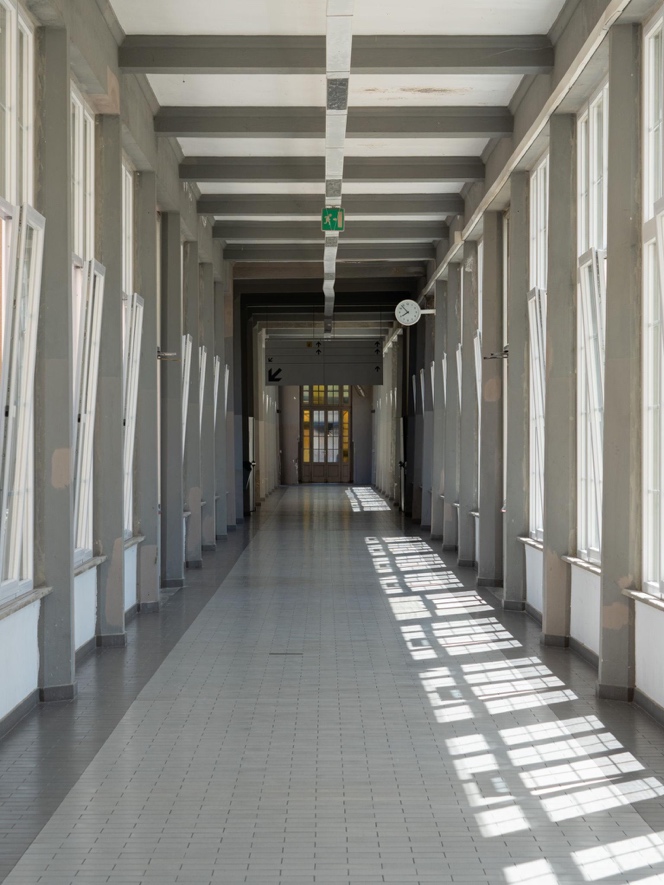 A quiet institutional hallway lit by window shadows